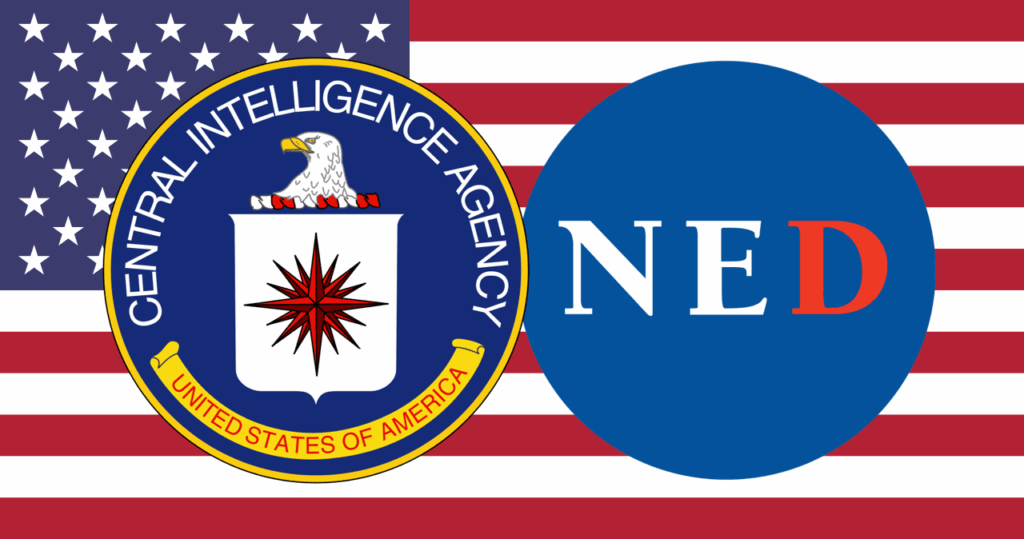 CIA and NED logos with the US flag in the background. Photo: CaitlinJohnstone.com/file photo.