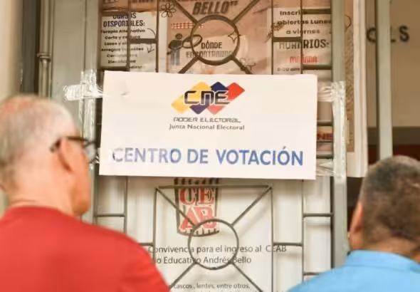 Two persons reading a National Electoral Council sign in front ot a voting center in Venezuela ahead of the May 25 elections. Photo: Telesur.