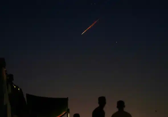 Displaced Palestinians stand outside tents as they watch trails of Iranian missiles targeting Israel, from Rafah's Mawasi area in the southern Gaza Strip on June 15, 2025. Photo: AFP.