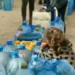A Palestinian girl sits amid several jars, waiting for her turn in a line to collect drinking water, in Gaza. Photo: Emad El Byed.