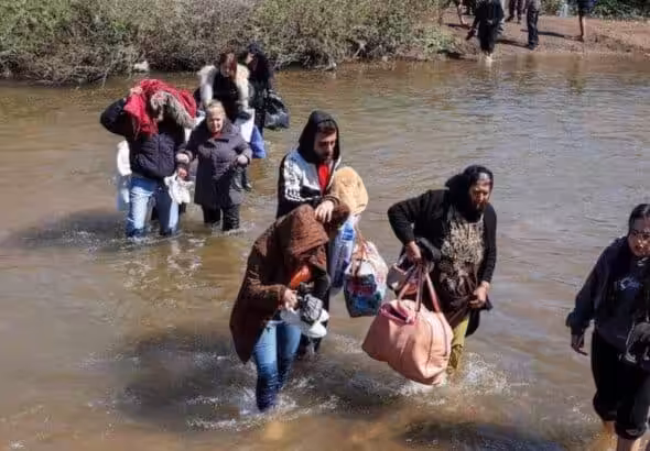 Alawite Syrians, who fled the violence in western Syria, walk in the water of the Nahr El Kabir River, after the mass killings of Alawite minority members, in Akkar, Lebanon on March 11, 2025. Photo: Reuters.