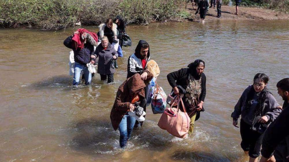 Alawite Syrians, who fled the violence in western Syria, walk in the water of the Nahr El Kabir River, after the mass killings of Alawite minority members, in Akkar, Lebanon on March 11, 2025. Photo: Reuters.