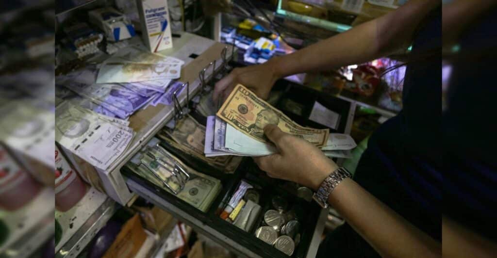 A person holds bolívar and US dollar bills above an open cash box. File photo.