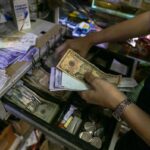 A person holds bolívar and US dollar bills above an open cash box. File photo.