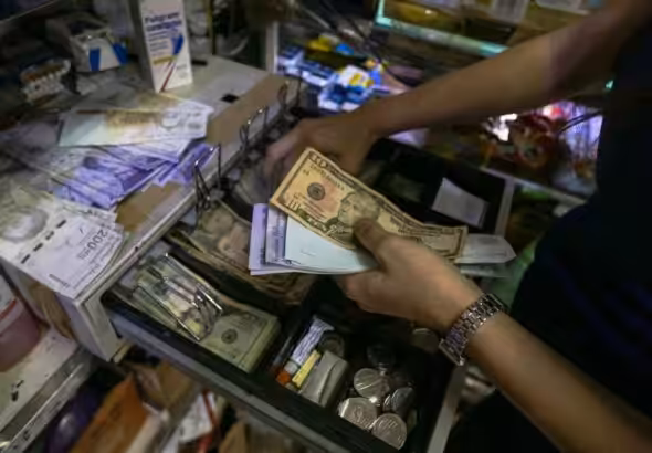 A person holds bolívar and US dollar bills above an open cash box. File photo.
