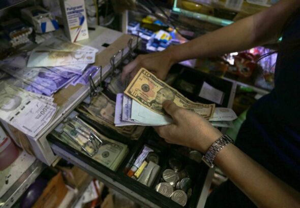A person holds bolívar and US dollar bills above an open cash box. File photo.