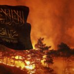 Image composition featuring flag of Saraya Ansar al-Sunnah flying in the foreground with a wildfire burning in the background. Photo: The Cradle.