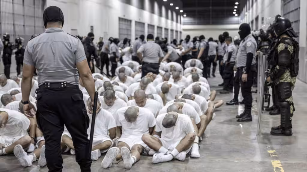 Inmates of the Salvadoran mega-prison CECOT sit on the floor while security personnel stand guard over them. Photo: France24.