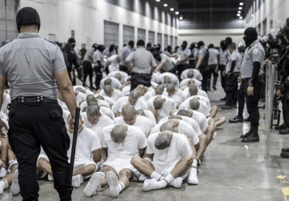 Inmates of the Salvadoran mega-prison CECOT sit on the floor while security personnel stand guard over them. Photo: France24.