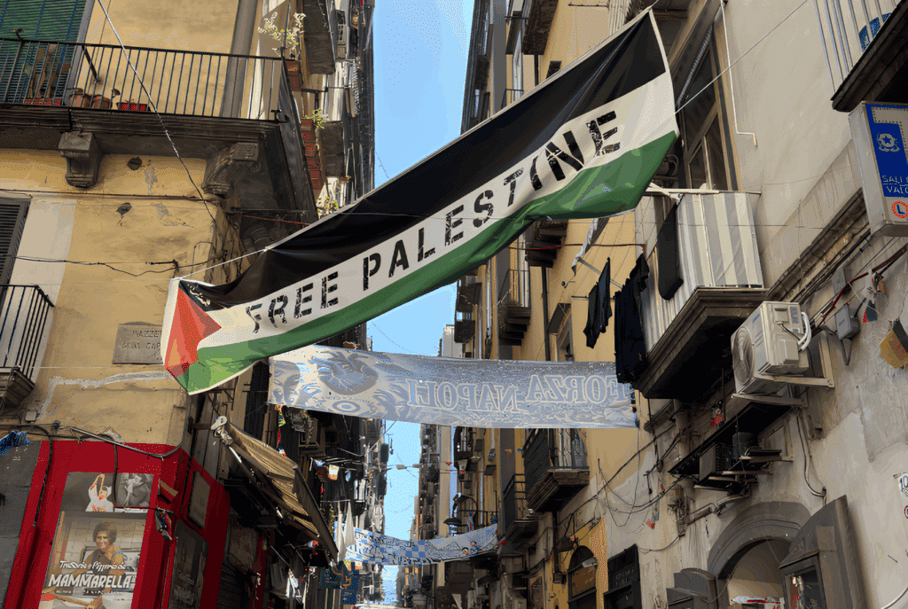 Palestinian flag flies in a street in Naples, Italy, with the words "Free Palestine" written on it. Photo: Zarefah Baroud/Palestine Chronicle.