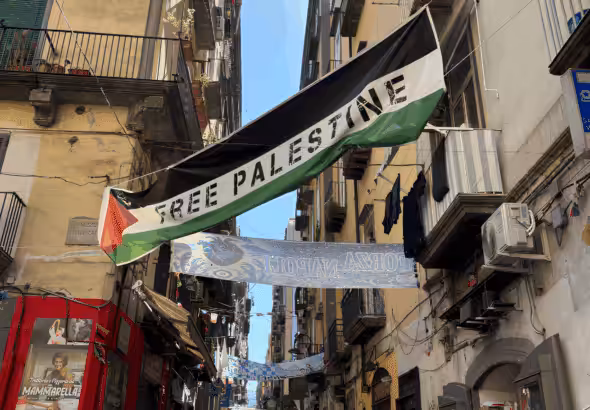 Palestinian flag flies in a street in Naples, Italy, with the words "Free Palestine" written on it. Photo: Zarefah Baroud/Palestine Chronicle.