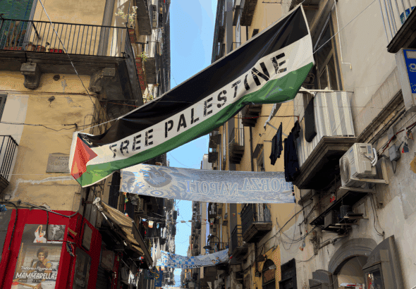 Palestinian flag flies in a street in Naples, Italy, with the words "Free Palestine" written on it. Photo: Zarefah Baroud/Palestine Chronicle.