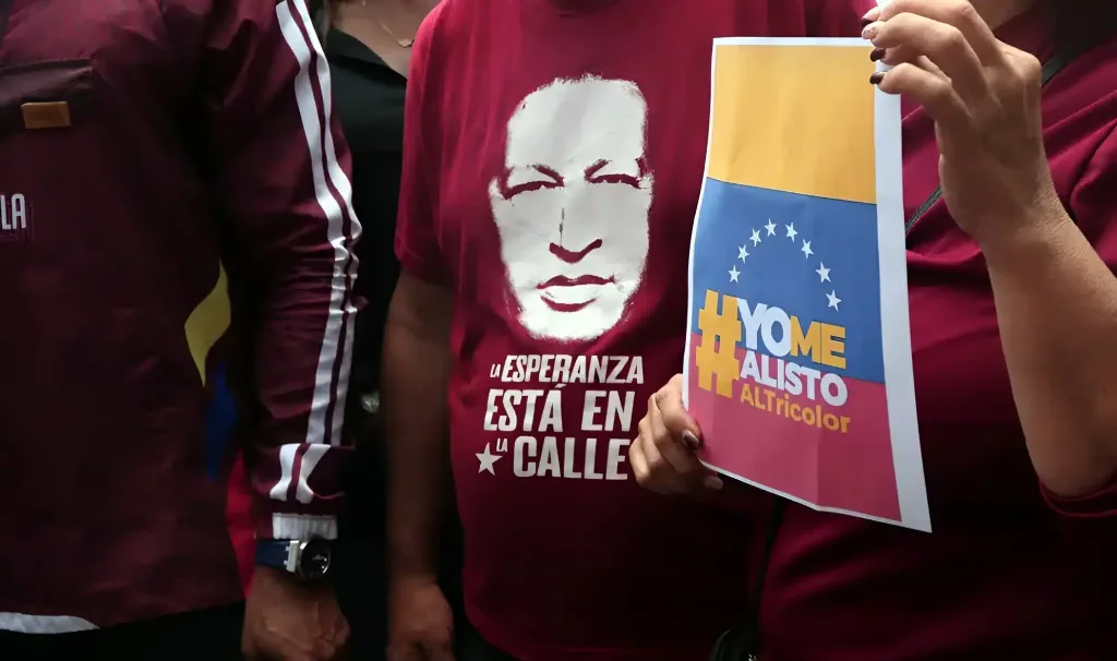 A person wears a t-shirt with the silhouette of President Hugo ChĂĄvez while another holds a paper sheet that reads "yo me enlisto" ("I am going to enlist"). Photo: Juan Carlos HernĂĄndez/contactophoto.