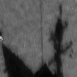 Black-and-white aerial photograph showing a small boat on the water and a large shadow of a US warship. Photo: Matias Delacroix/Associated Press.