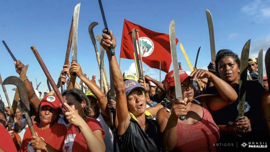 Women members of Brazil’s Landless Rural Workers’ Movement (MST) hold their scythes and machetes aloft. Photo: Brasil Paralelo.