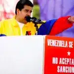 The image shows Venezuelan President Nicolás Maduro at a political rally. He is standing behind a podium with signs that read "Venezuela Se Respeta" and "No Aceptamos Sanciones." These Spanish phrases translate to "Venezuela is respected" and "We do not accept sanctions". Photo: Venezuela Analysis.
