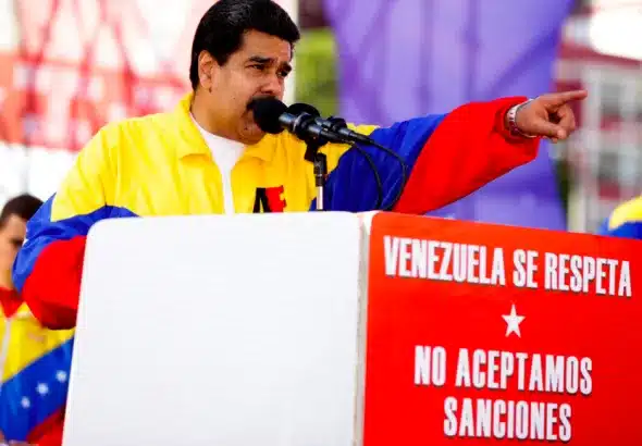 The image shows Venezuelan President Nicolás Maduro at a political rally. He is standing behind a podium with signs that read "Venezuela Se Respeta" and "No Aceptamos Sanciones." These Spanish phrases translate to "Venezuela is respected" and "We do not accept sanctions". Photo: Venezuela Analysis.