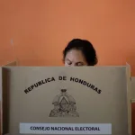 A person participates in an election in Honduras, using a voting booth provided by the National Electoral Council. The booth displays the coat of arms and name of the Republic of Honduras. Photo: Jorge Cabrera/Reuters/file photo.