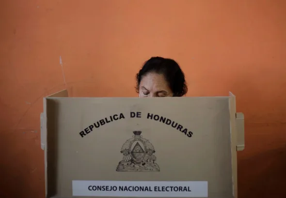 A person participates in an election in Honduras, using a voting booth provided by the National Electoral Council. The booth displays the coat of arms and name of the Republic of Honduras. Photo: Jorge Cabrera/Reuters/file photo.