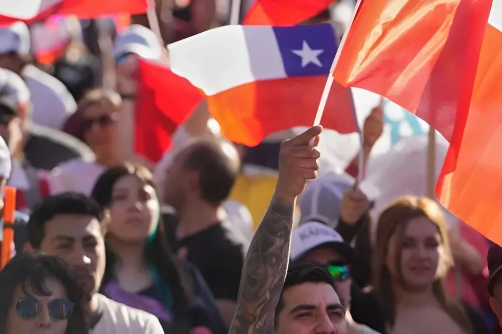 A crowd gathered at a political campaign event in Chile, specifically one of the final rallies for the presidential election held in November 2025. The people in the image are waving the national flags of Chile. Photo: Esteban Félix/AP.