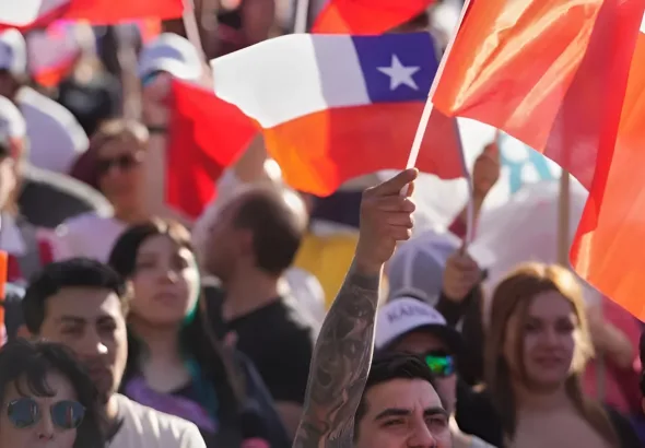 A crowd gathered at a political campaign event in Chile, specifically one of the final rallies for the presidential election held in November 2025. The people in the image are waving the national flags of Chile. Photo: Esteban Félix/AP.