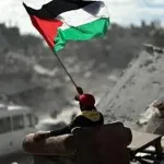 A Palestinian child raises the flag over the ruins of his home — a reminder that no imposed plan can extinguish the struggle for self-determination. Photo: Struggle La Lucha.
