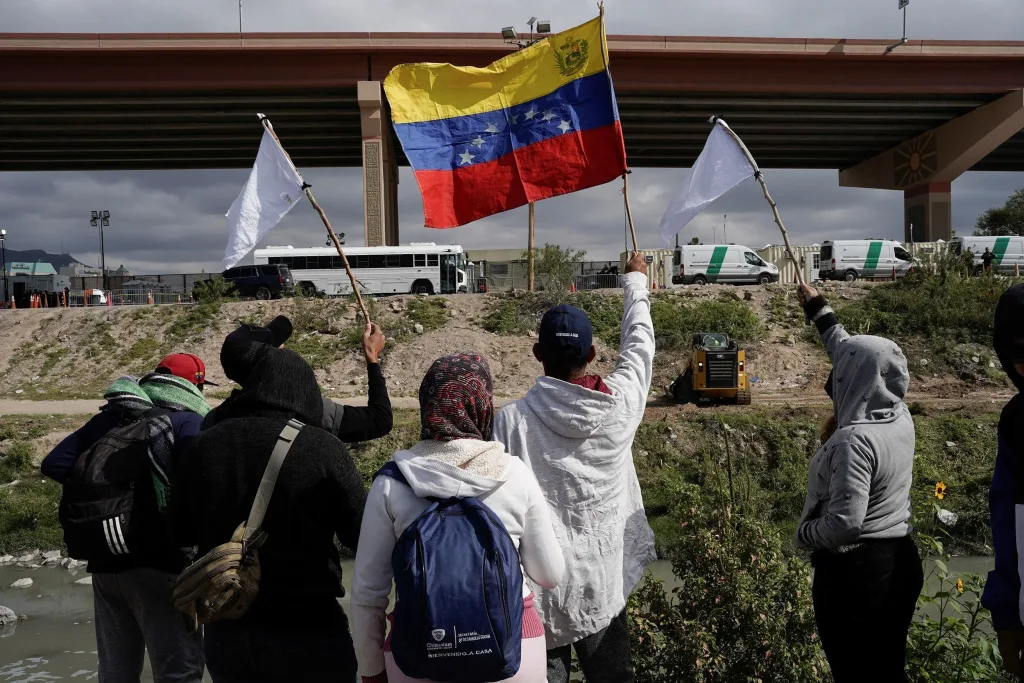 2022 photo of Venezuelan migrants, some who were expelled back to Mexico, and others who arrived in Juarez and haven't crossed yet, wave flags on the banks of the Rio Grande while peacefully protesting new US migration enforcement rules. Photo: Paul Ratje/Reuters/file photo.