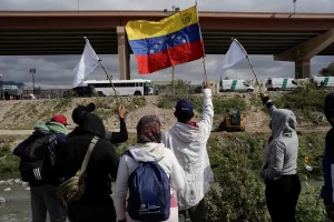 2022 photo of Venezuelan migrants, some who were expelled back to Mexico, and others who arrived in Juarez and haven't crossed yet, wave flags on the banks of the Rio Grande while peacefully protesting new US migration enforcement rules. Photo: Paul Ratje/Reuters/file photo.