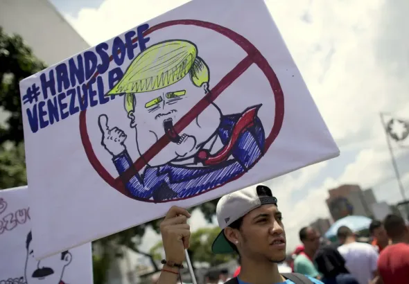 A protester holds a "Hands Off Venezuela" poster at an anti-imperialist protest in Caracas, Venezuela. Photo: AP/Ariana Cubillos.