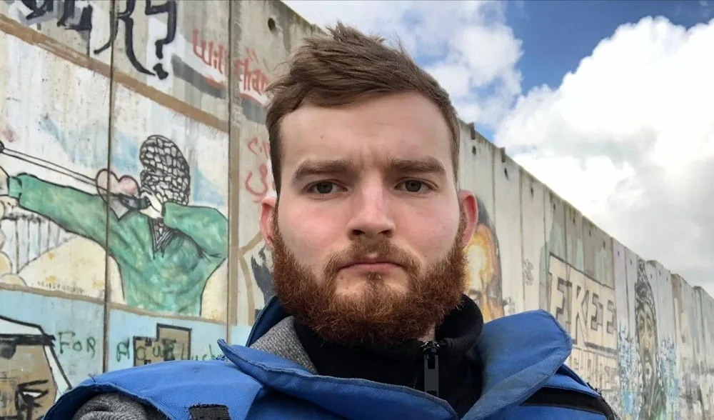 Robert Inlakesh in front of the separation wall at the Qalandia checkpoint, occupied West Bank, in February 2020. Photo: Robert Inlakesh/file photo.