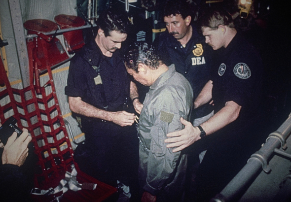Manuel Antonio Noriega watches as U.S. Drug Enforcement Agents place chains around his waist aboard a C-130 transport plane on Jan. 4, 1990. Noriega surrendered to U.S. authorities in Panama City and was flown to Miami, Florida, where he faced drug trafficking charges. Photo: AP.