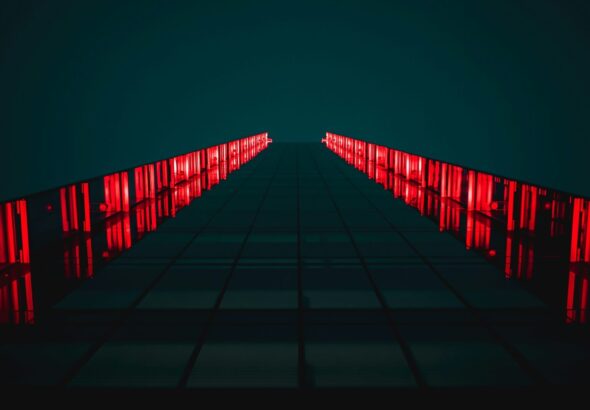 low-angle photograph of a modern building facade at night, illuminated by bright red vertical lights. Photo: Tanner Boriack.
