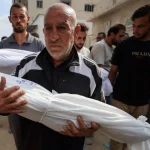 A man carries the body of a child killed by the Israeli army at a funeral in Gaza City. Photo: Dawoud Abu Alkas/Reuters.