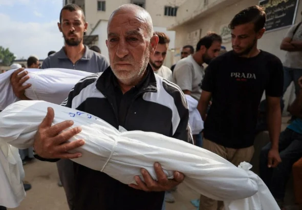 A man carries the body of a child killed by the Israeli army at a funeral in Gaza City. Photo: Dawoud Abu Alkas/Reuters.