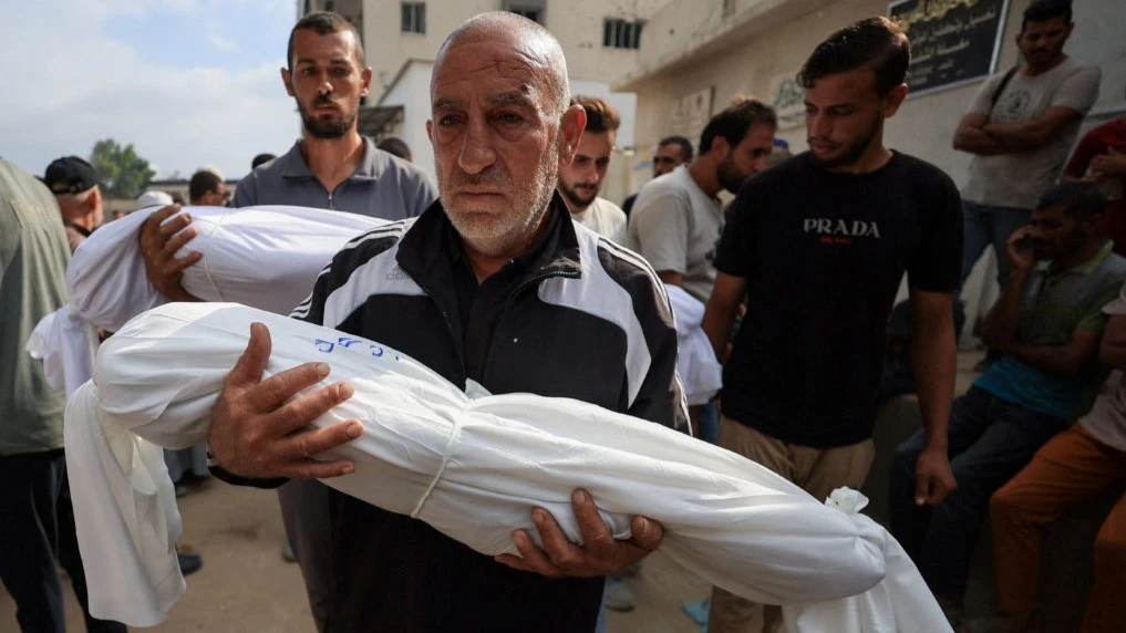 A man carries the body of a child killed by the Israeli army at a funeral in Gaza City. Photo: Dawoud Abu Alkas/Reuters.