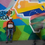 A man sells phone cables in front of a mural of the Venezuelan map with the Essequibo territory included in the Petare neighborhood of Caracas, Venezuela, in December 2023. Photo: Matias Delacroix/AP.