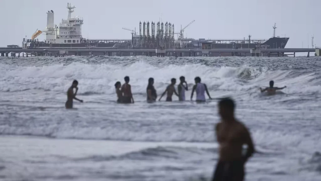 People bathing in the ocean against the backdrop of an oil tanker moored at the El Palito refinery complex, in Carabobo state of Venezuela. Photo: Jesús Vargas/Getty Images.