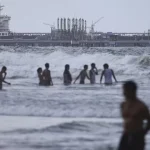 People bathing in the ocean against the backdrop of an oil tanker moored at the El Palito refinery complex, in Carabobo state of Venezuela. Photo: Jesús Vargas/Getty Images.