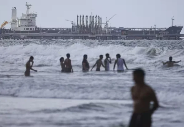 People bathing in the ocean against the backdrop of an oil tanker moored at the El Palito refinery complex, in Carabobo state of Venezuela. Photo: Jesús Vargas/Getty Images.