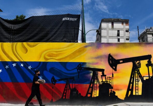 A man wearing a face mask walks past a mural depicting an oil pump and the Venezuelan flag in a street of Caracas, on May 26, 2022. Photo: Federico Parra/AFP/file photo.
