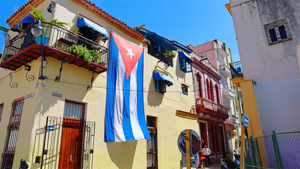 A typical street scene in Old Havana, Cuba, featuring distinctive colonial architecture and a large Cuban flag displayed on a building. Photo: Cigar Aficionado/file photo.