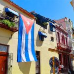 A typical street scene in Old Havana, Cuba, featuring distinctive colonial architecture and a large Cuban flag displayed on a building. Photo: Cigar Aficionado/file photo.