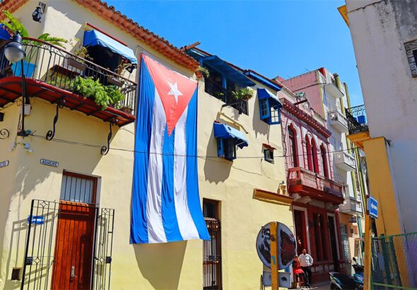 A typical street scene in Old Havana, Cuba, featuring distinctive colonial architecture and a large Cuban flag displayed on a building. Photo: Cigar Aficionado/file photo.
