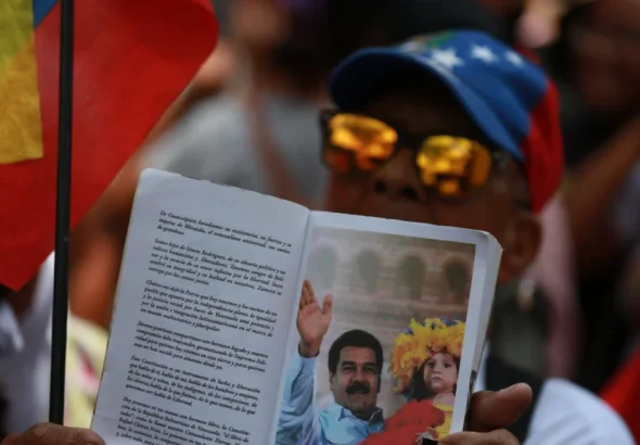 A marcher holds a book open on a page showing a photo of Venezuelan President Nicolás Maduro, in Caracas, March 12, 2026. Photo: Ricardo Malik/Telesur.