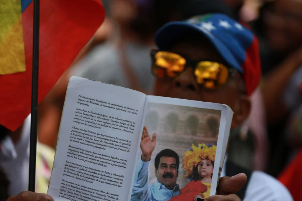 A marcher holds a book open on a page showing a photo of Venezuelan President Nicolás Maduro, in Caracas, March 12, 2026. Photo: Ricardo Malik/Telesur.