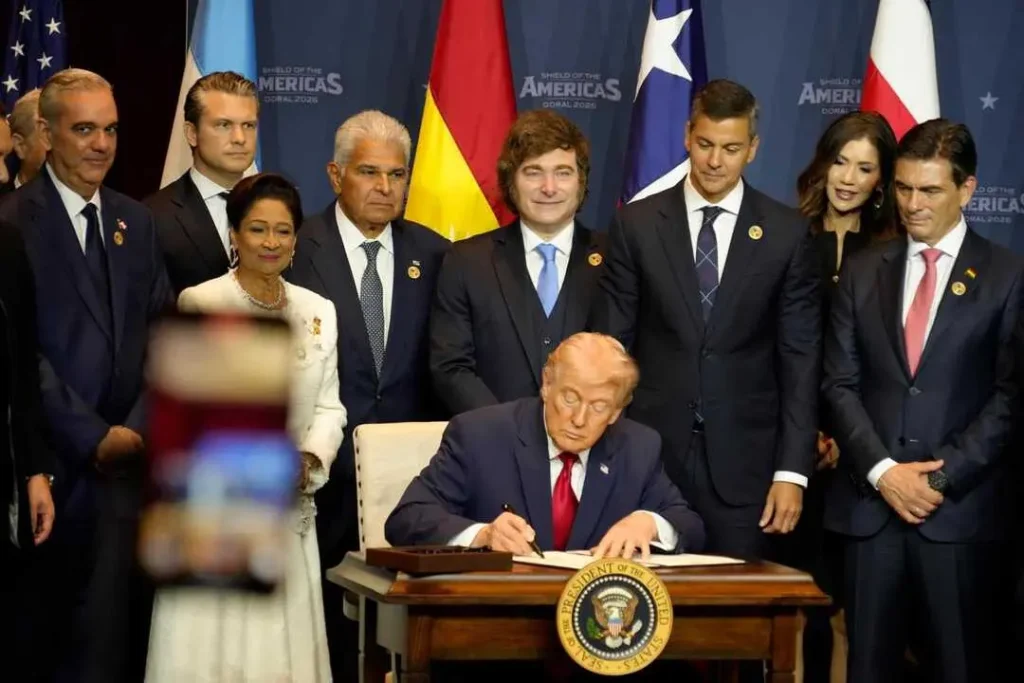 Argentinian President Javier Milei standing behind US President Donald Trump who signs the declaration of the Shield of the Americas summit in Miami. Photo: X/@JMilei.