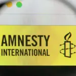 An Amnesty International logo seen through a magnifier. Photo: Casimiro/Alamy/file photo.