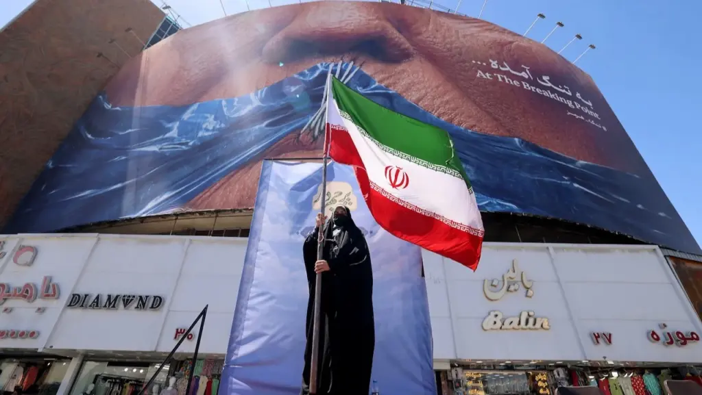A political rally or demonstration in Iran, featuring a large mural and a person holding the Iranian flag. Photo: Atta Kenare/AFP/Getty Images.