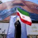A political rally or demonstration in Iran, featuring a large mural and a person holding the Iranian flag. Photo: Atta Kenare/AFP/Getty Images.