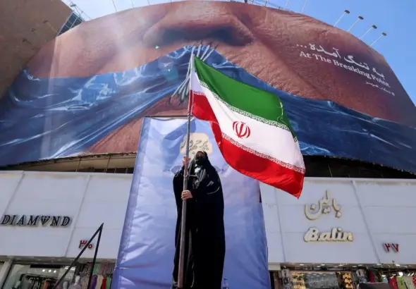 A political rally or demonstration in Iran, featuring a large mural and a person holding the Iranian flag. Photo: Atta Kenare/AFP/Getty Images.